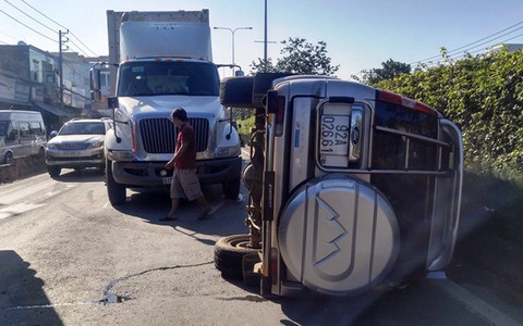 Lật ngang trước đầu xe container, ba người trong xe hơi bò ra